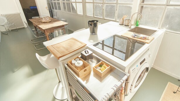 A compact kitchen with a built-in washer and dryer, a wooden dining table, and a window with a view.