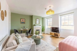 A living room with a sofa, a coffee table, a fireplace, a television, and a dining area with chairs and a table. - Charming Studio| Windsor Castle Views By Tempstay (Windsor)
