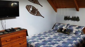 A bedroom with a bed, a wooden dresser, a flat-screen TV, and wall decorations.