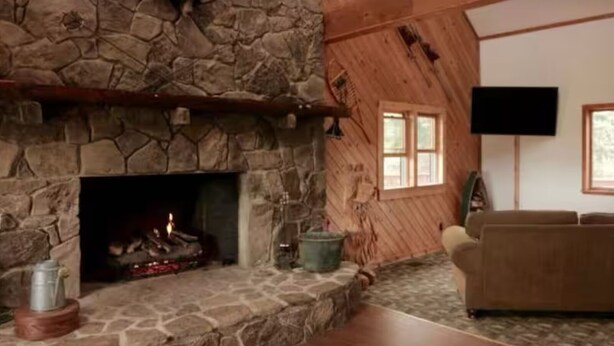 A stone fireplace with a fire, a wooden wall, a window, and a flat-screen TV mounted on the wall.