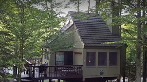 A small cabin with a deck, surrounded by trees.