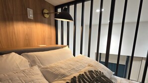Habitación de hotel con cama, un ventanal con persianas, un reloj de pared y una lámpara en el techo.