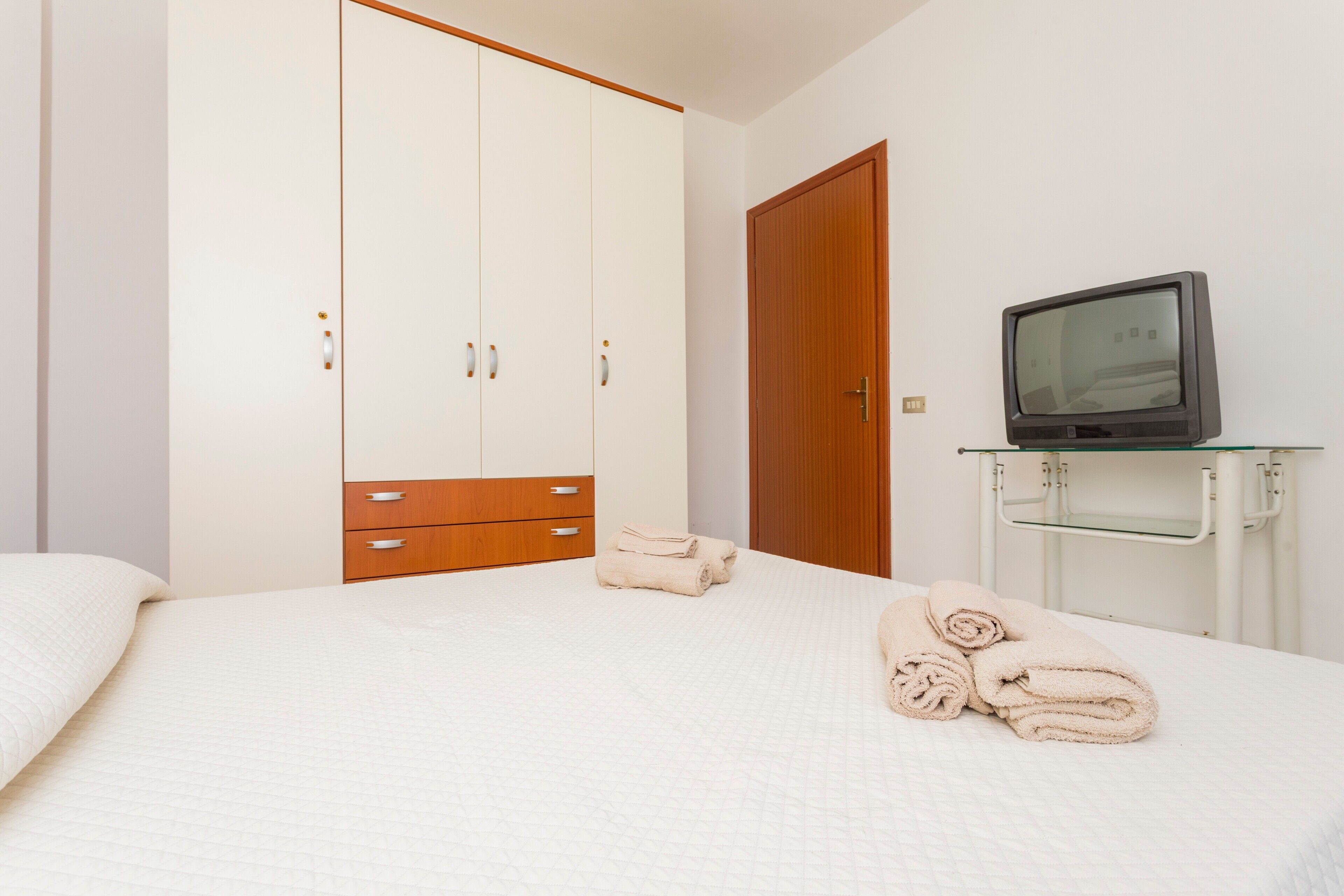 Une chambre à coucher avec un lit, une armoire, un téléviseur posé sur un meuble et des serviettes sur le lit.