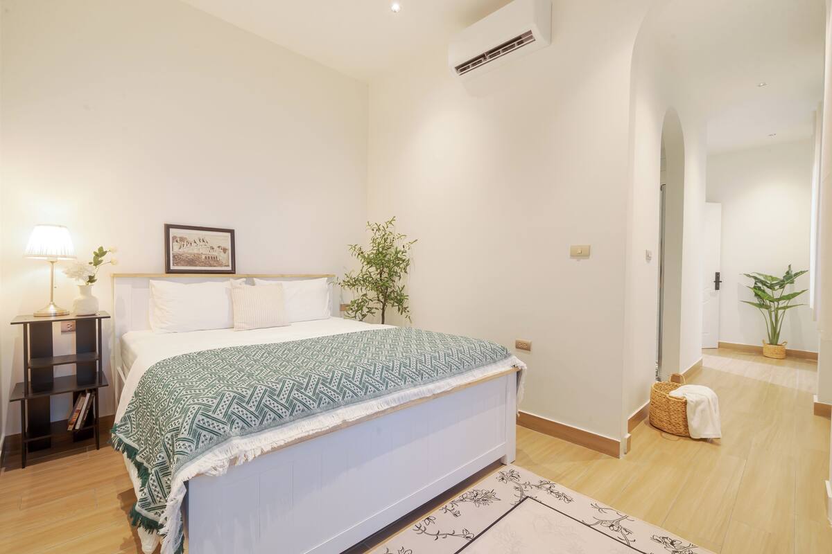 A bedroom with a bed, bedside table, lamp, and a framed picture on the wall.