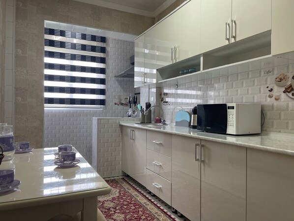 A modern kitchen with white cabinets, a built-in microwave, and a window with blinds.