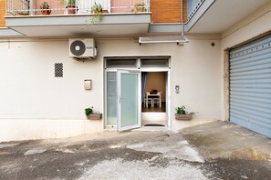 Un immeuble résidentiel doté d’une porte coulissante à l’entrée, d’une petite table et d’une chaise à l’intérieur, et de plantes en pot sur le balcon.