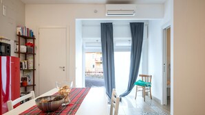 Un comedor con una mesa dispuesta para dos, un refrigerador rojo, una estantería y vistas a través de un vano.