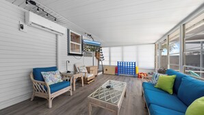 Une vaste terrasse dotée d’un canapé bleu, de fauteuils en osier, d’une table basse en verre et offrant une vue sur l’extérieur.