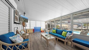 Une pièce lumineuse, baignée de soleil, avec une grande fenêtre, un canapé bleu, des fauteuils en osier et une table basse en verre.
