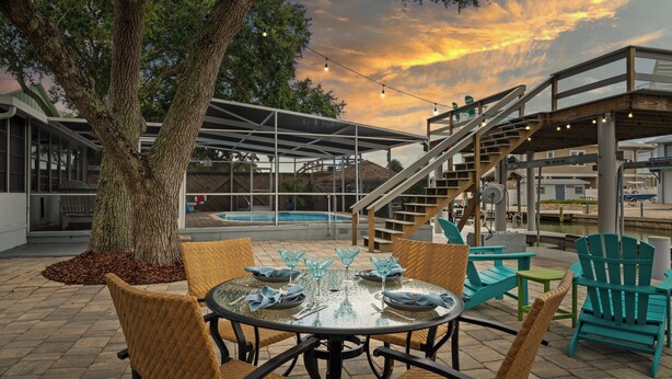Une terrasse extérieure avec une table ronde dressée pour le repas, entourée de chaises en osier et une piscine en arrière-plan.