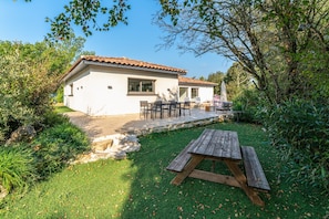 Una casa con patio, una mesa de madera y un jardín.