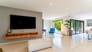 A modern living room with a flat-screen TV, a white sofa, a wooden console, and a large window.