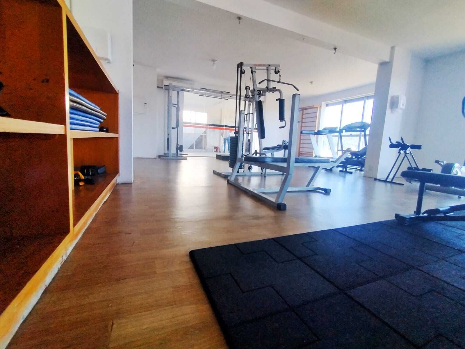 Een sportschool met houten vloer, trainingsapparatuur en een groot raam.