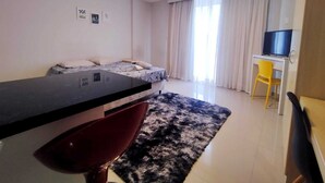 Habitación de hotel moderna con cama, escritorio con silla, televisor y ventana grande con cortinas.