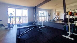Un gimnasio amplio con diversos equipos de ejercicio, ventanas grandes y un espejo que refleja el espacio.