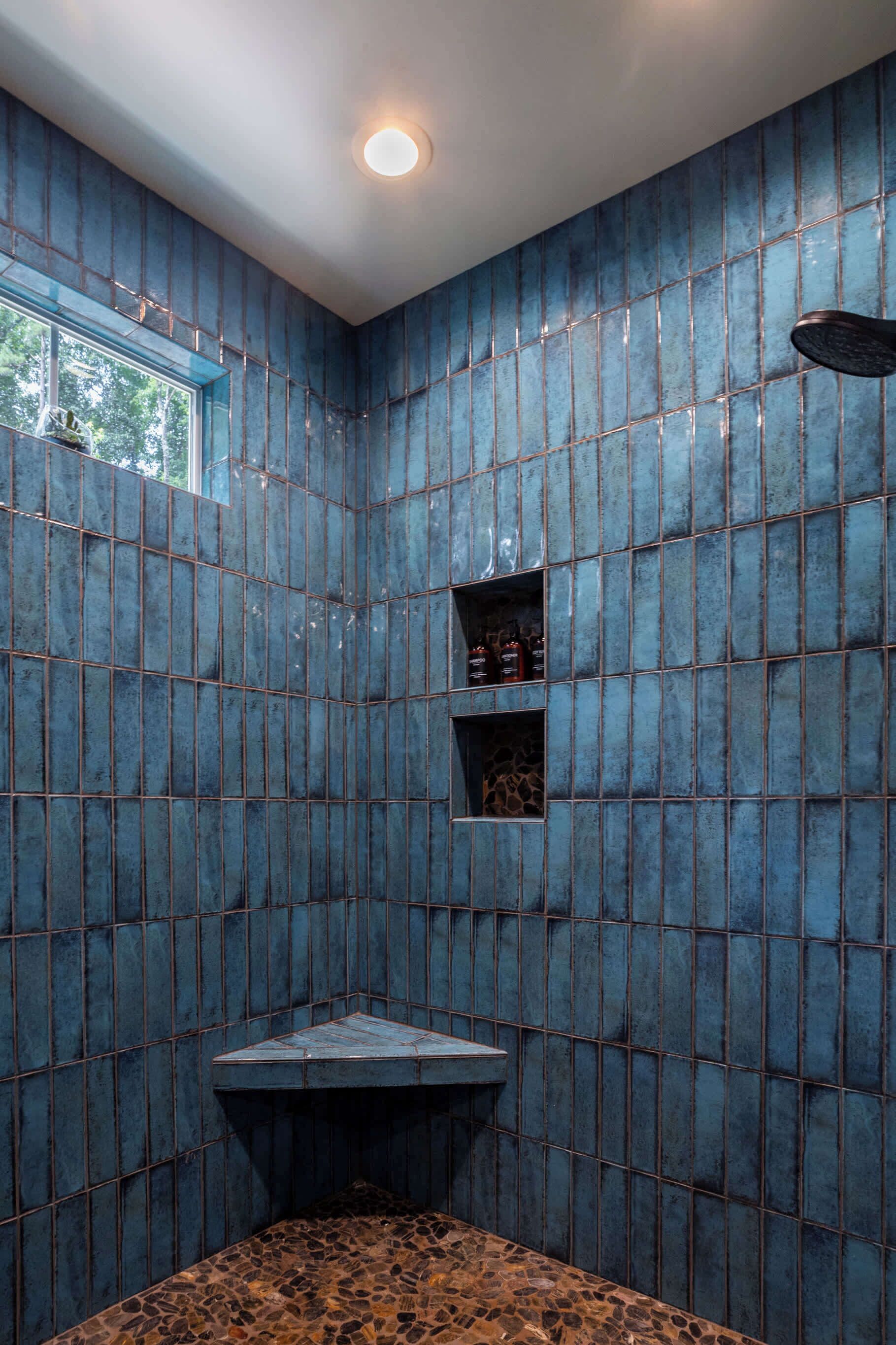 Une salle de bain avec des murs recouverts de carreaux bleus, une fenêtre et une douche.