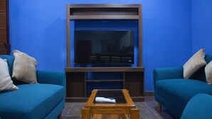 A living room with two teal sofas, a wooden coffee table, and a large flat-screen TV mounted on a wooden entertainment unit.