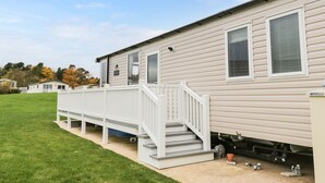 A single-story mobile home with a white exterior, a front porch with a white railing, and a small front yard. - Kelly's Retreat (Scarborough)