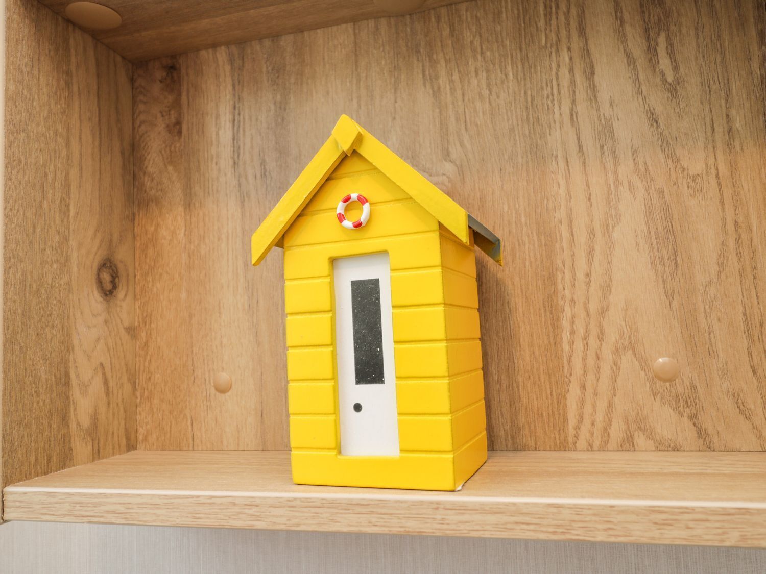 A small yellow wooden structure resembling a house with a white door and a lifebuoy on top.