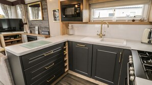 A modern kitchen with dark cabinetry, a white countertop, a stainless steel stove, and a window above the sink. - Kelly's Retreat (Scarborough)