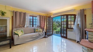 A living room with a sofa, a coffee table, a plant, and a view through a glass door. - Lemon Green Apartment (Celle Ligure)