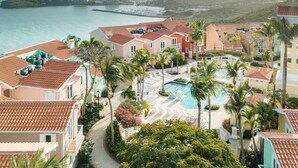A resort with a swimming pool, palm trees, and a view of the ocean and mountains. - Brisas Del Mar | Stunning Views & Best Location (Fajardo)