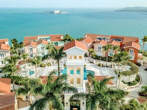 Un resort con piscina central, palmeras y vistas al océano.