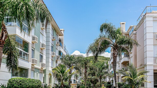 Un immeuble d’appartements moderne doté de balcons, entouré d’une végétation luxuriante et de palmiers.