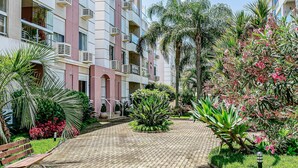 Une cour dotée d’une allée pavée, de bancs et d’une végétation luxuriante, notamment des palmiers et des plantes à fleurs.
