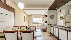 Un coin repas avec une table et des chaises, une cuisine équipée de placards et d’un réfrigérateur, et une vue sur l’extérieur par une porte vitrée.