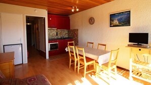 A compact living space with a dining area, kitchen, and a TV on a stand.