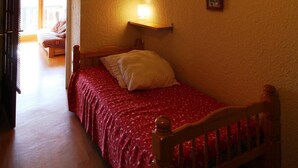 A bedroom with a single bed, a bedside lamp, a wooden headboard, and a small shelf with pictures.