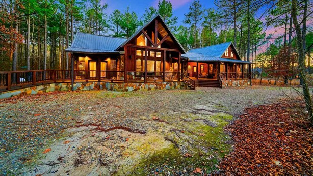 A lodge with a stone foundation, wooden exterior, and a metal roof, surrounded by a forested area.