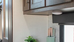 A kitchenette with wooden cabinets, a white countertop, a potted plant, and a window with a view.