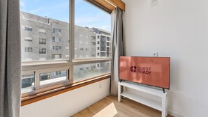 Une chambre d’hôtel dotée d’une grande fenêtre, d’un téléviseur à écran plat posé sur un meuble et offrant une vue sur un immeuble à plusieurs étages.