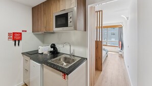 Une cuisine compacte équipée d’un four à micro-ondes, d’un évier et d’une machine à café. On y trouve des placards en bois et un petit réfrigérateur. Un extincteur est fixé au mur.