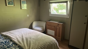 A bedroom with a bed, a chair, a wooden cabinet, and a window with a view of trees. - Guest Room with Lake View, Wi-Fi, and Air Conditioning (Arles)