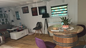 A living room with a wooden floor, a round wooden table, a purple chair, a white sofa, a black floor lamp, and a potted plant. - Guest Room with Lake View, Wi-Fi, and Air Conditioning (Arles)