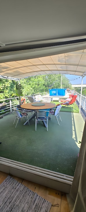 A covered outdoor area with a round table and chairs, a blue container, and a red chair. - Guest Room with Lake View, Wi-Fi, and Air Conditioning (Arles)
