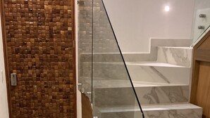 Un escalier avec des rampes en verre et des marches en marbre, menant à une porte en bois ornée d’un motif en mosaïque.