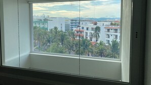 Une pièce dotée d’une grande fenêtre donnant sur un paysage urbain avec des immeubles et des palmiers.