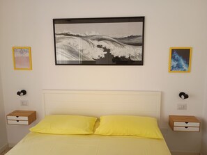 A bedroom with a bed, two bedside tables, and two framed artworks on the wall.