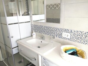 A bathroom with a white sink, a mirror, and a shower enclosure.
