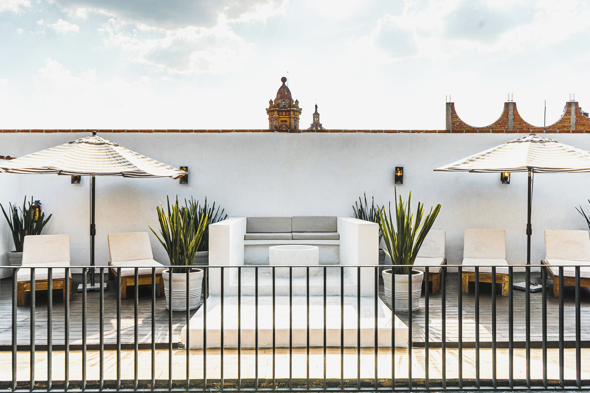 A rooftop terrace with outdoor seating, potted plants, and a view of a historic building.