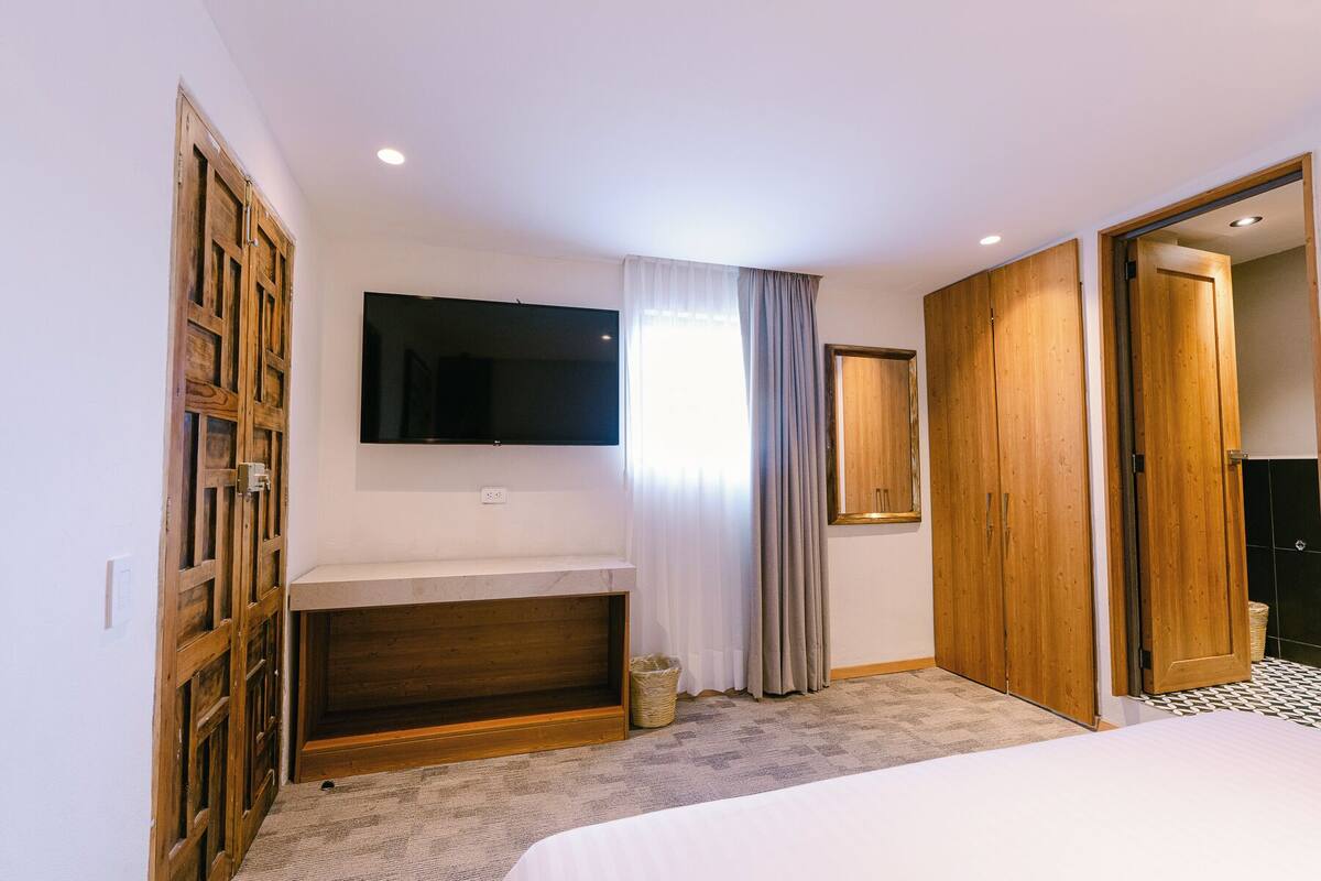 A bedroom with a bed, a TV mounted on the wall, a wooden wardrobe, and a mirror.