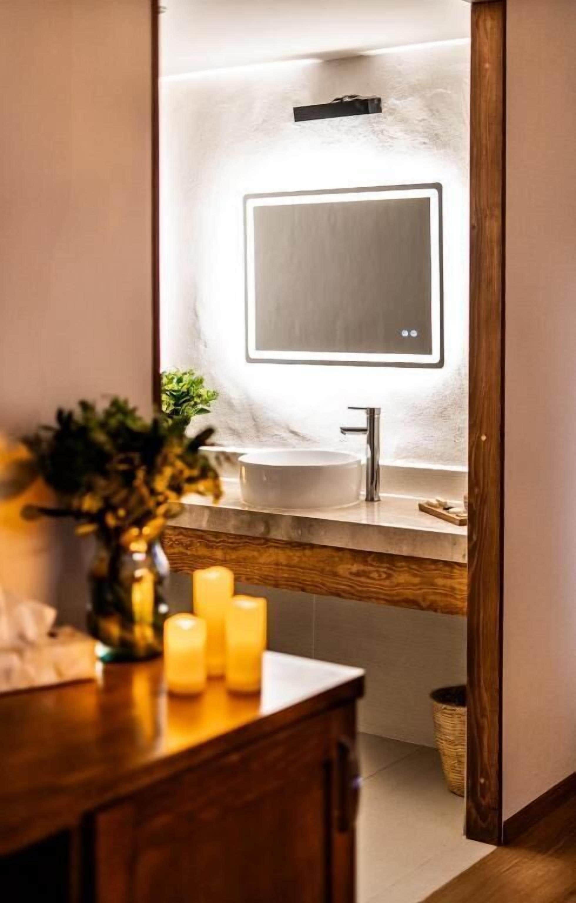 Een badkamer met een houten wastafel, een witte wasbak, een spiegel en kaarsen.