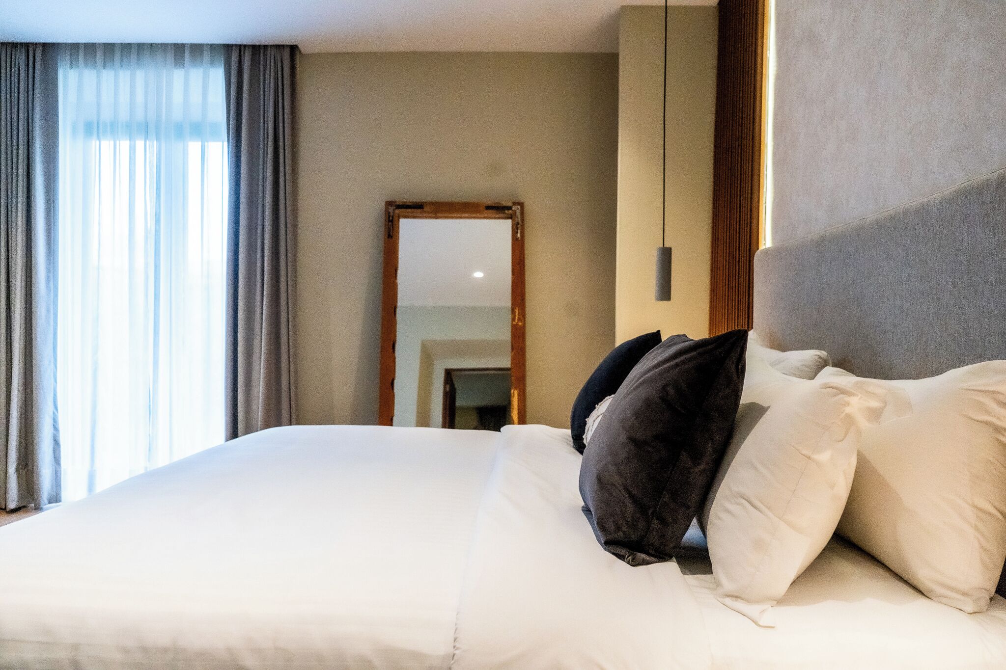 Ein Hotelzimmer mit einem großen Bett, einem Spiegel und Blick ins Freie durch transparente Vorhänge.