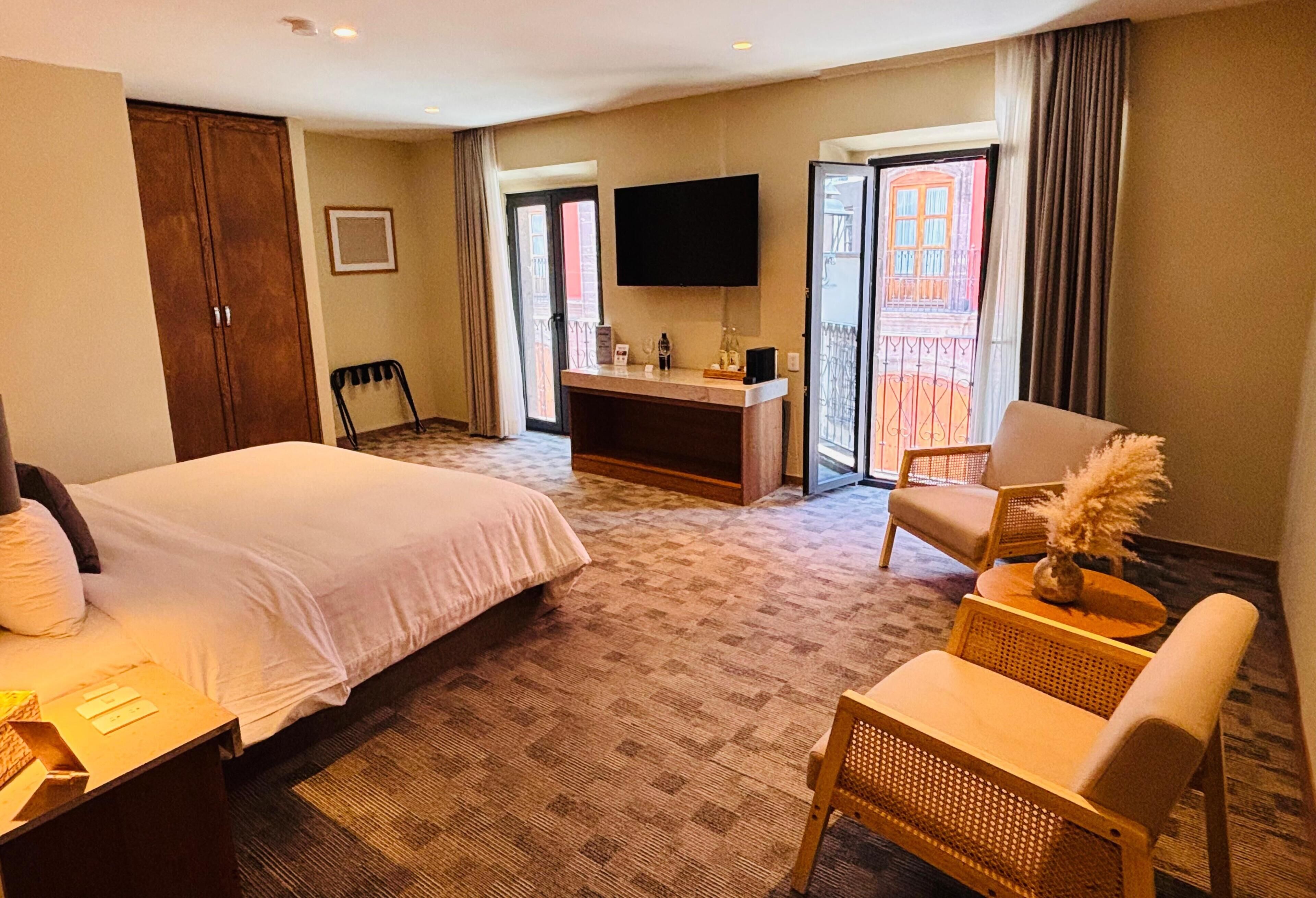 A hotel room with a bed, a desk, a chair, a TV, and a balcony with a view.