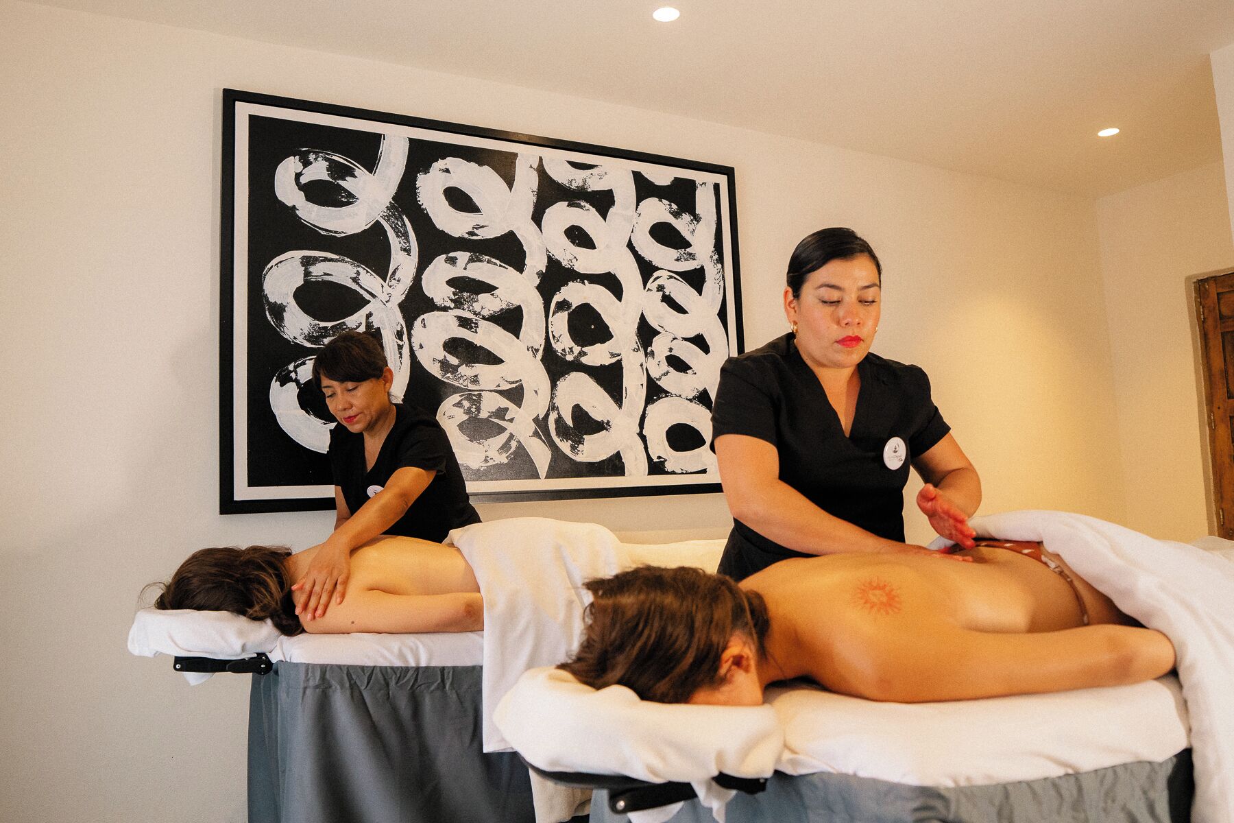 Un cuarto de terapia de masajes con dos clientes recibiendo masajes en la espalda.