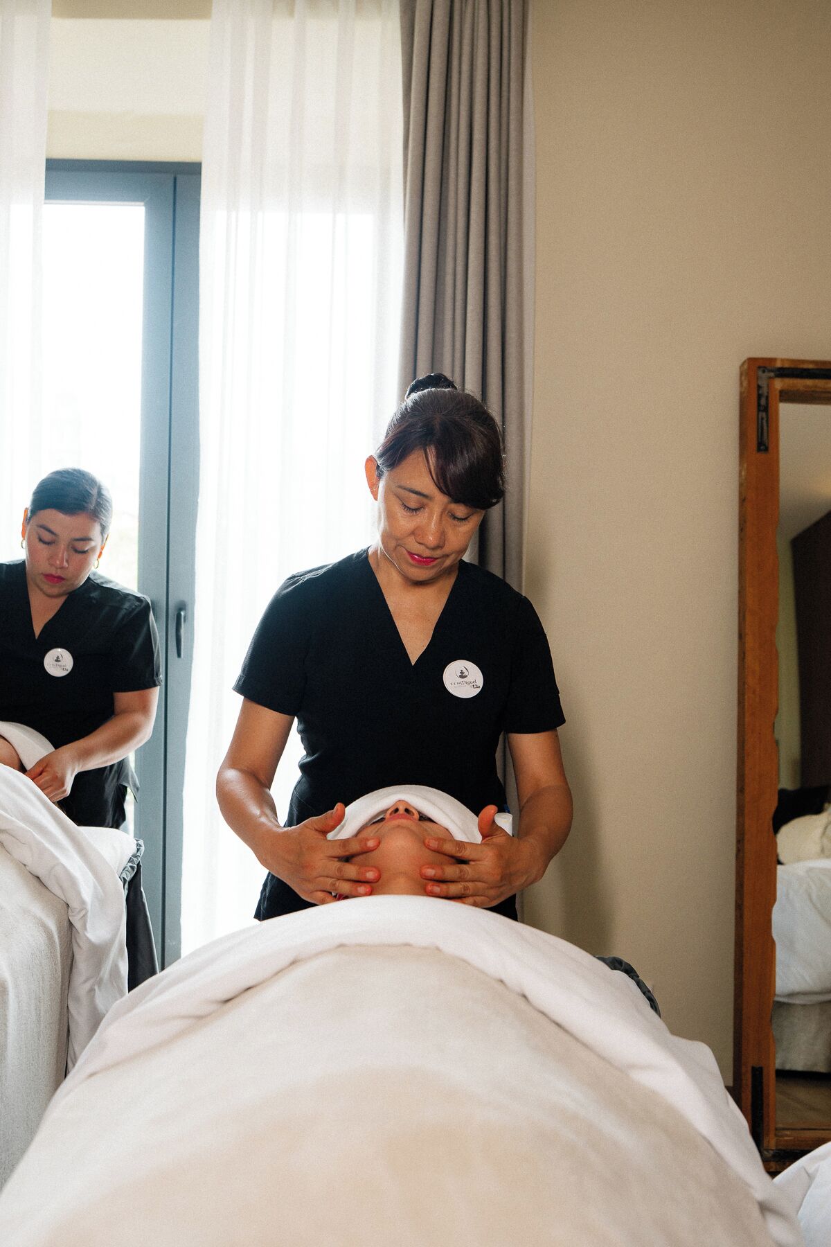 Sesión de masoterapia en una habitación con cama, puerta de madera y ventana con cortinas.